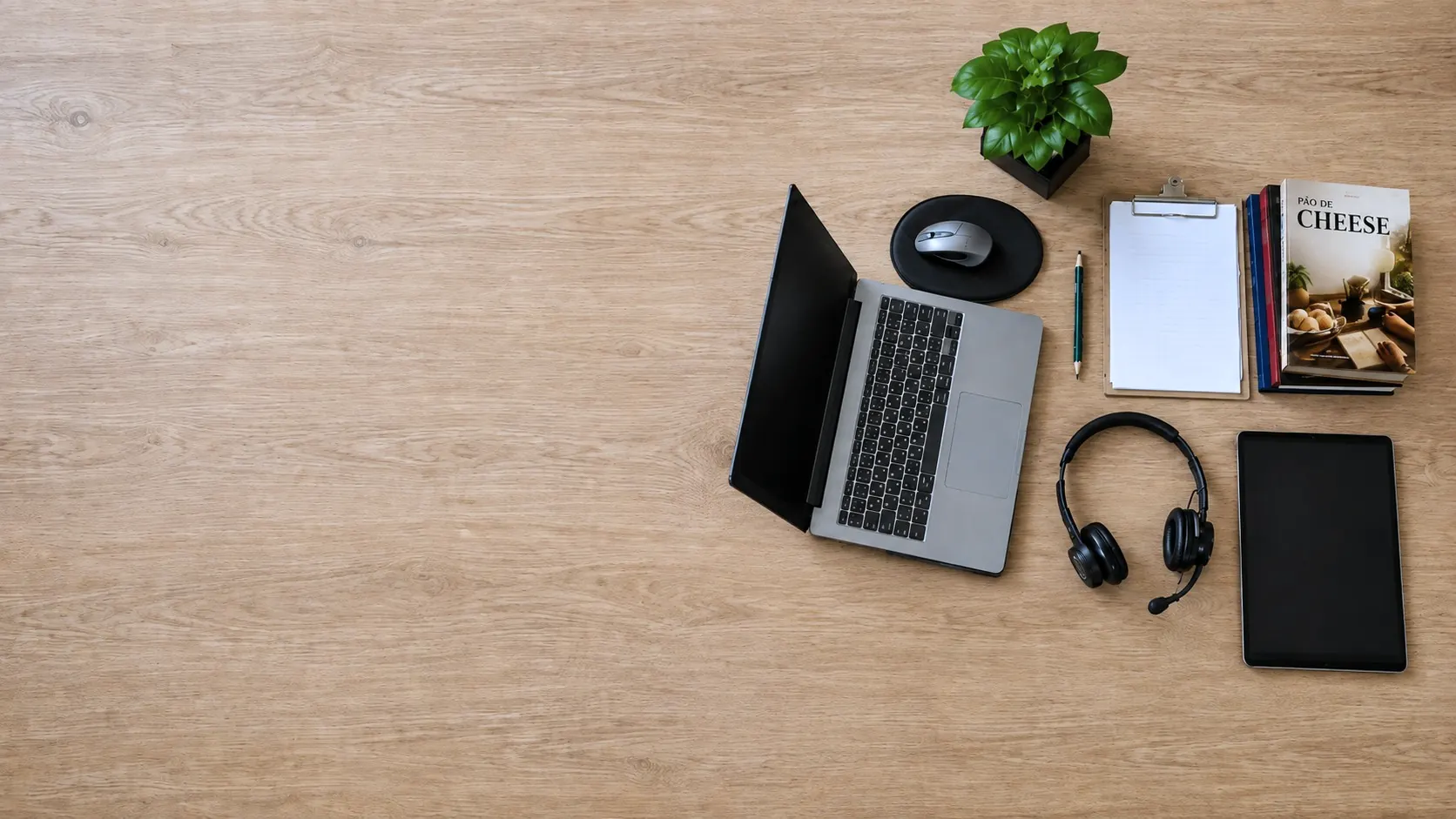 Vista de cima da mesa de trabalho do professor: laptop aberto, headset, prancheta e o livro Pão de Cheese
